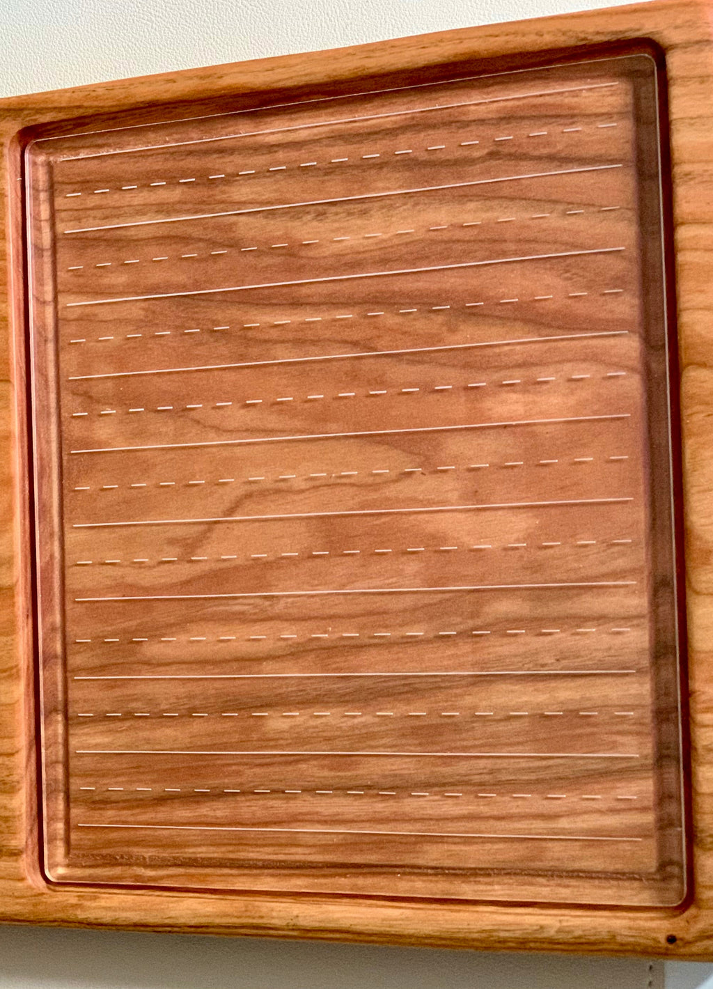 Wooden-framed clear board with horizontal dashed and solid lines for handwriting or calligraphy practice on wood surface