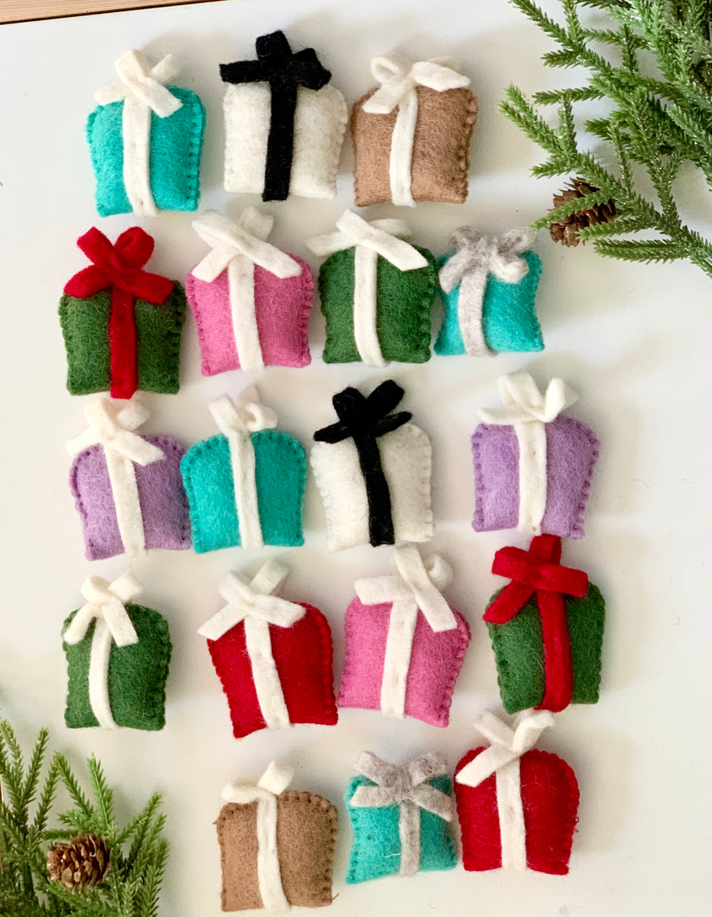 Felt holiday gift boxes in various colors with sewn white, black, red, and gray ribbon bows on white background with pine branches