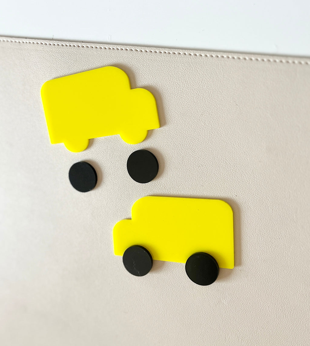 Two simple yellow truck-shaped pieces with separate black circular wheels on a light beige textured surface
