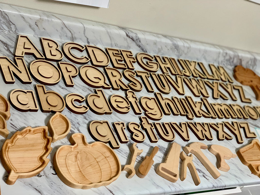 Laser cut wooden uppercase and lowercase alphabet letters with pumpkin, leaf, and tool-shaped sensory trays on marble surface