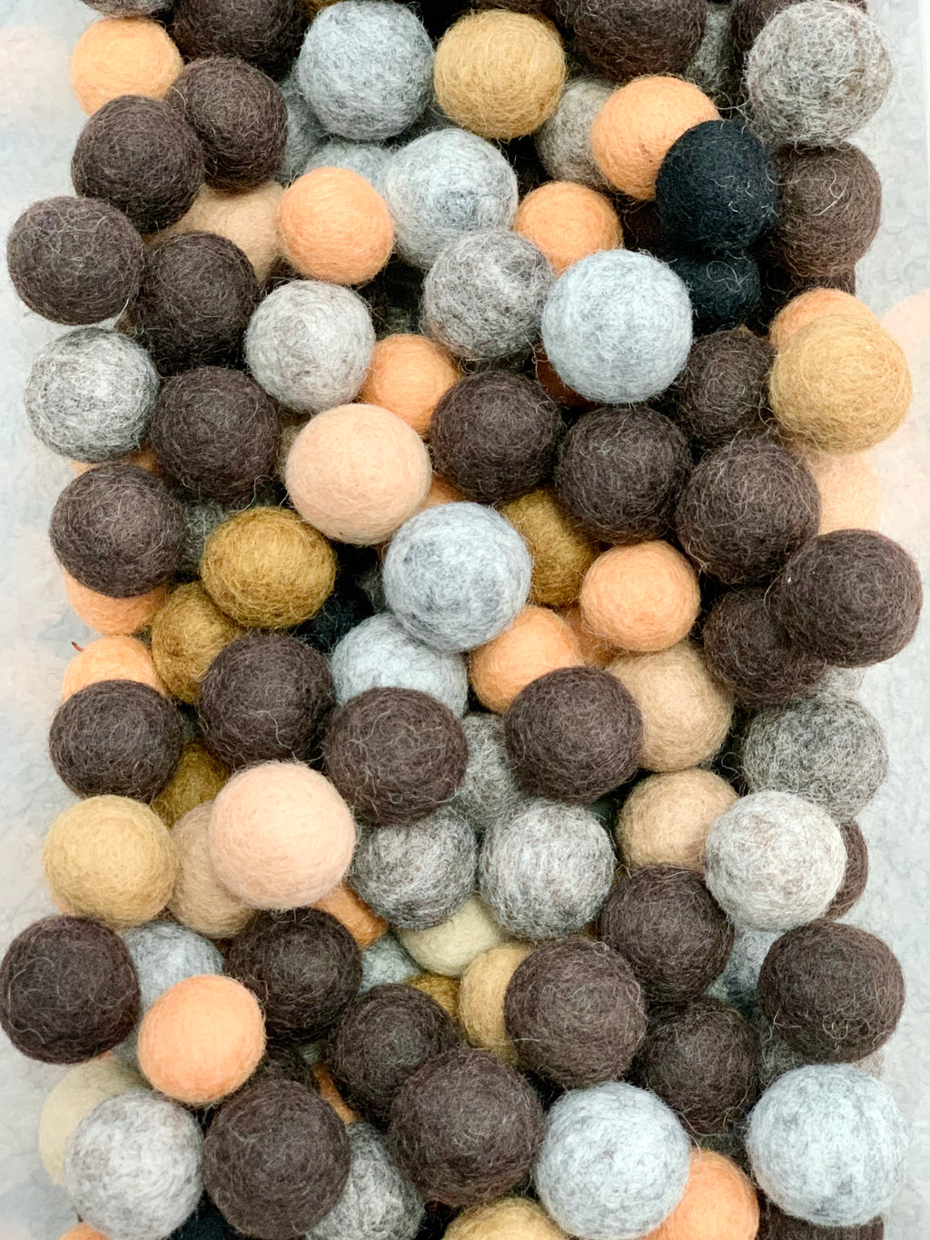 Assortment of earth-toned and neutral felt balls in various soft natural shades displayed closely together