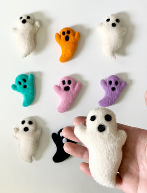 Assortment of colorful handmade felt ghost figures in white, orange, teal, pink, purple, and black on white background