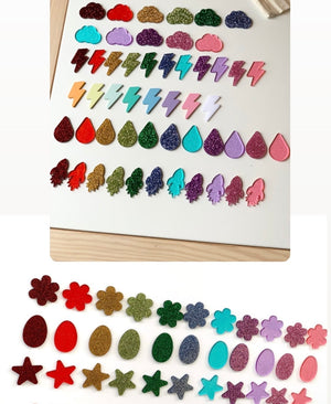 Rows of colorful glittery plastic shapes including clouds, lightning bolts, water drops, and rockets arranged on a white surface