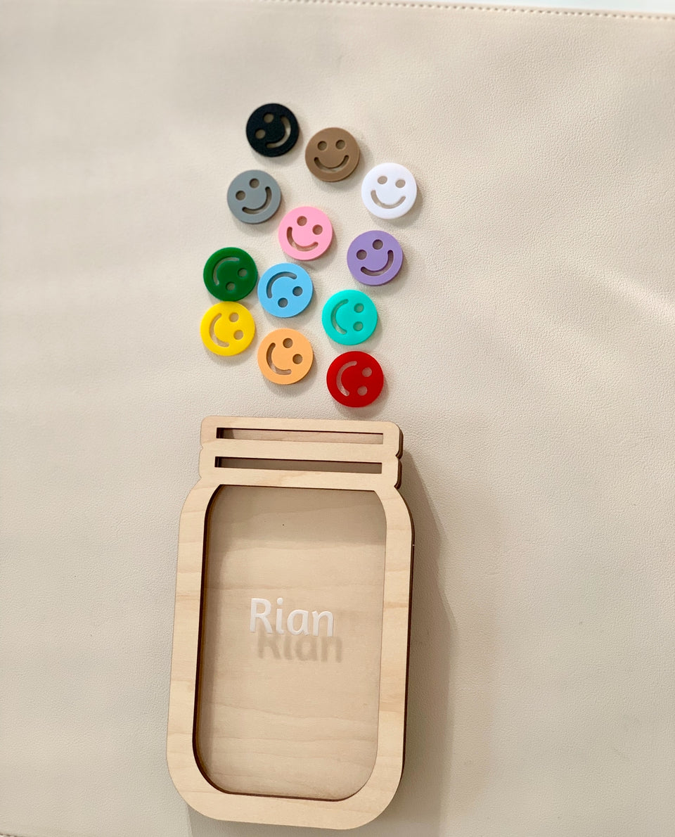 Wooden personalized reward jar with engraved name and colorful smiley face tokens on light background