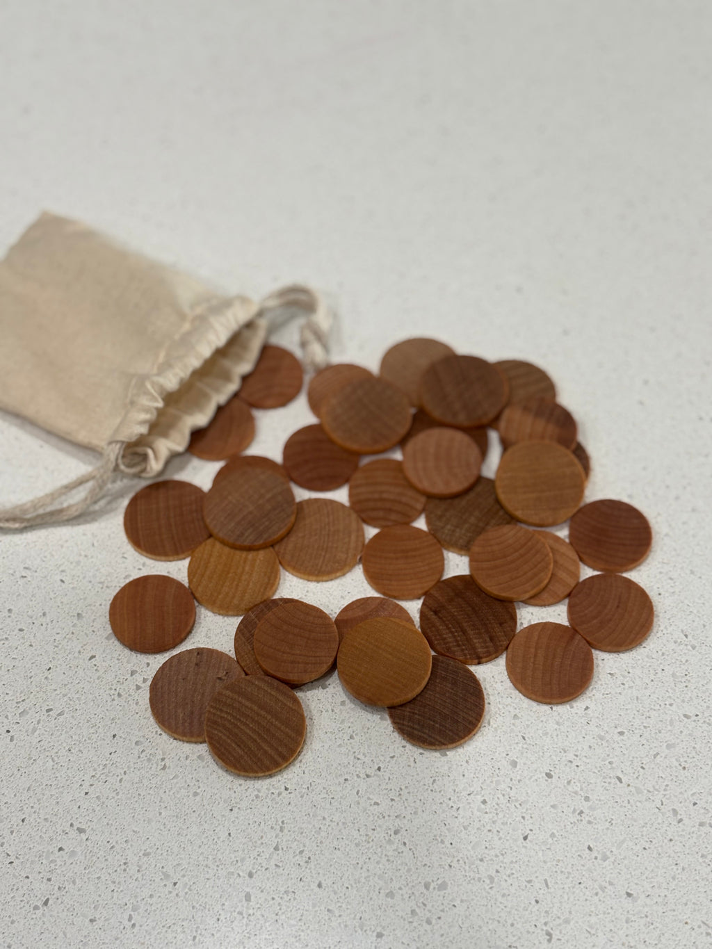 Small round wooden tokens scattered beside a beige drawstring fabric pouch on a light surface