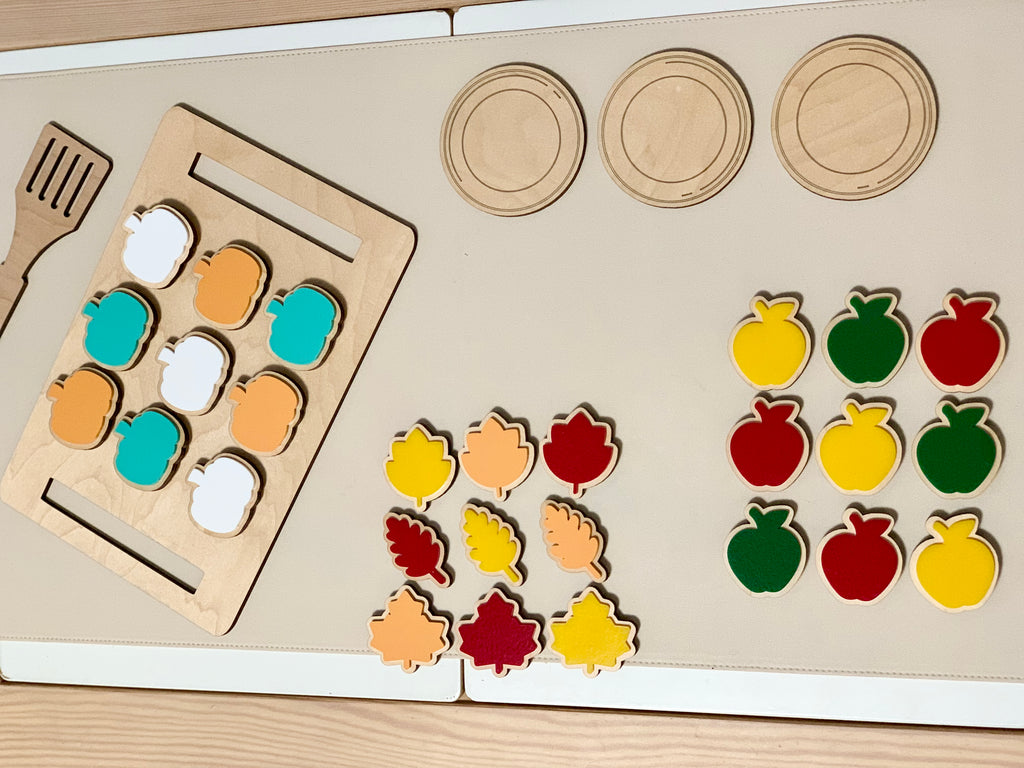 Wooden cookie sheet with velcro cookies in fall shapes next to wooden plates and spatula on beige mat