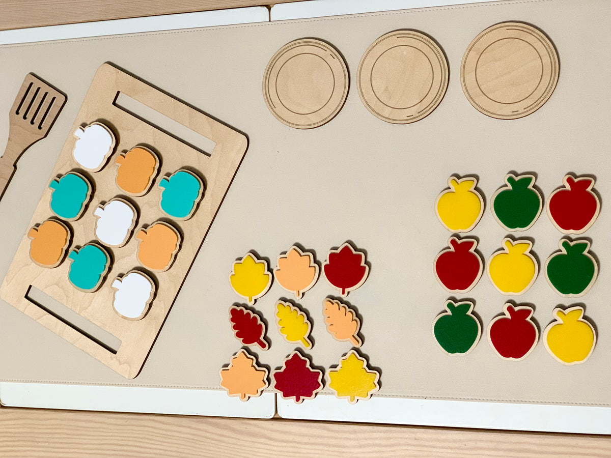 Wooden cookie sheet with velcro cookies in fall shapes next to wooden plates and spatula on beige mat