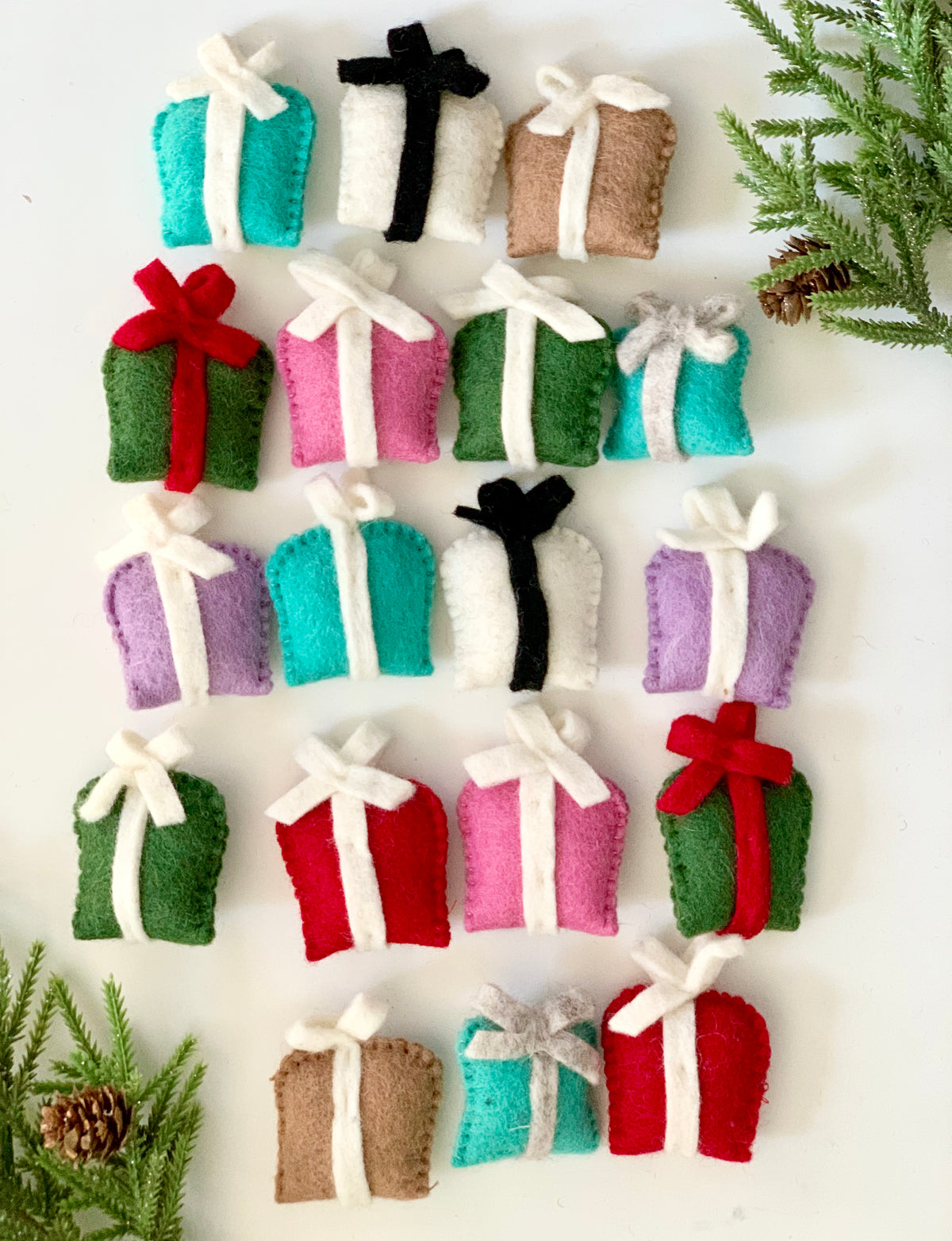 Hand-stitched felt gift boxes in assorted colors with contrasting ribbon bows displayed on white background with pine sprigs