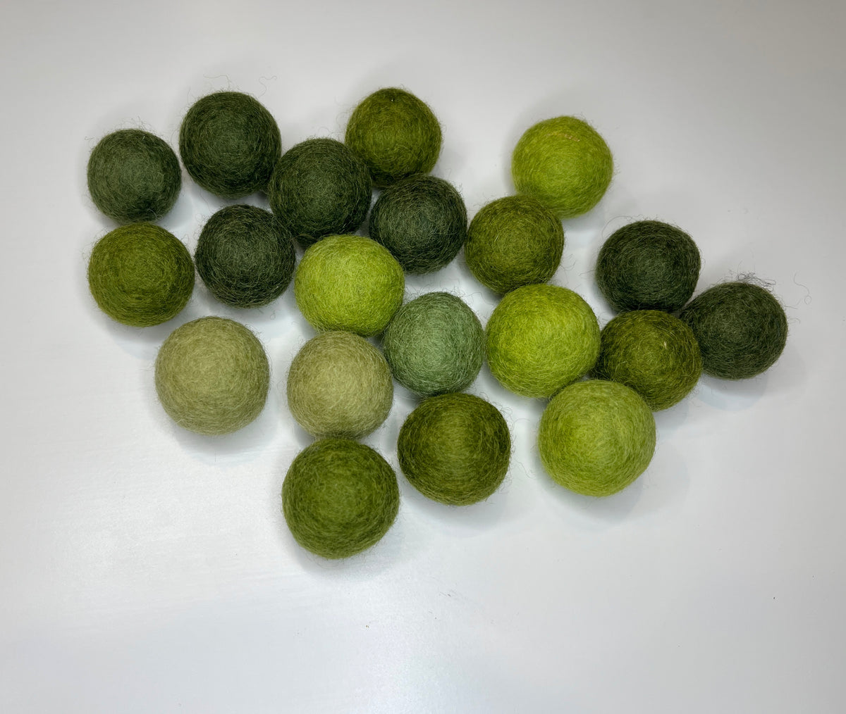 Assortment of 20 felt balls in varying shades of green on white background