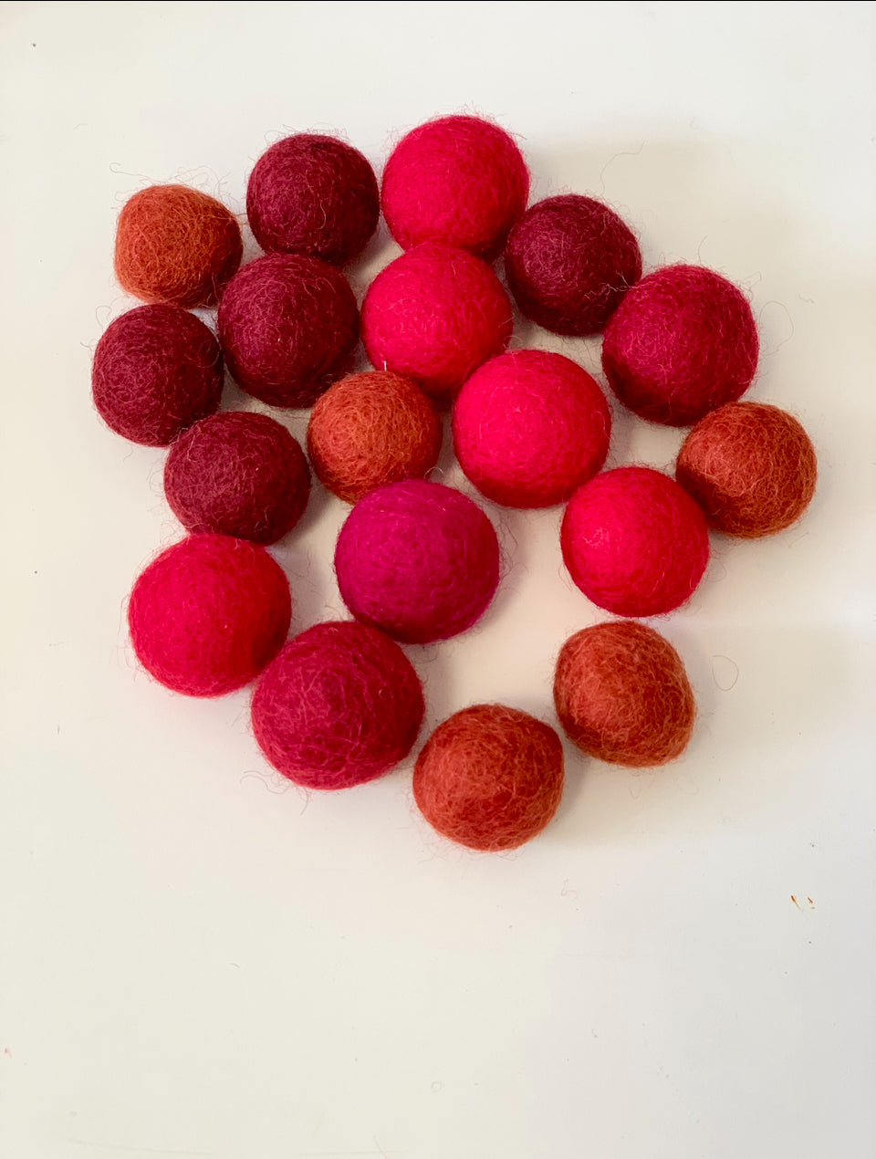 Assortment of 18 felt balls in various red tones arranged on a white background