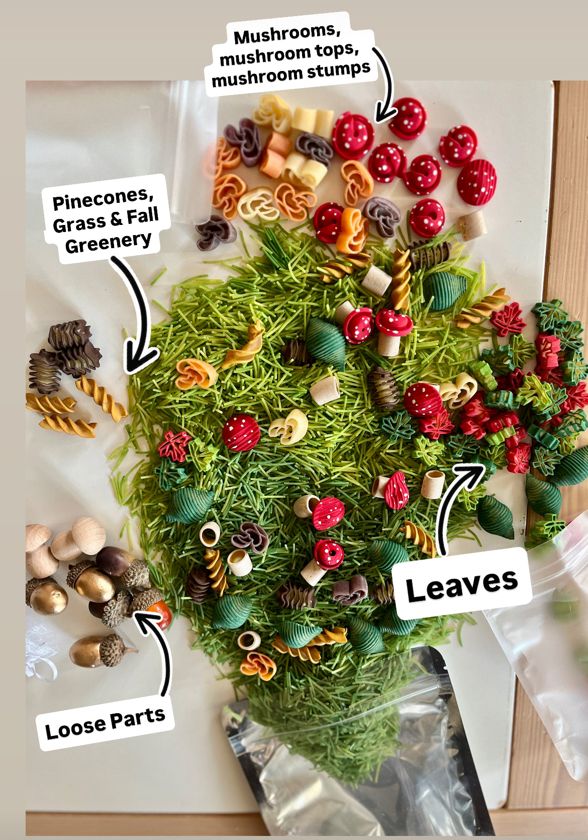 Colorful pasta shapes mixed with wooden acorns, pinecones, and fall-themed craft leaves on green shredded grass