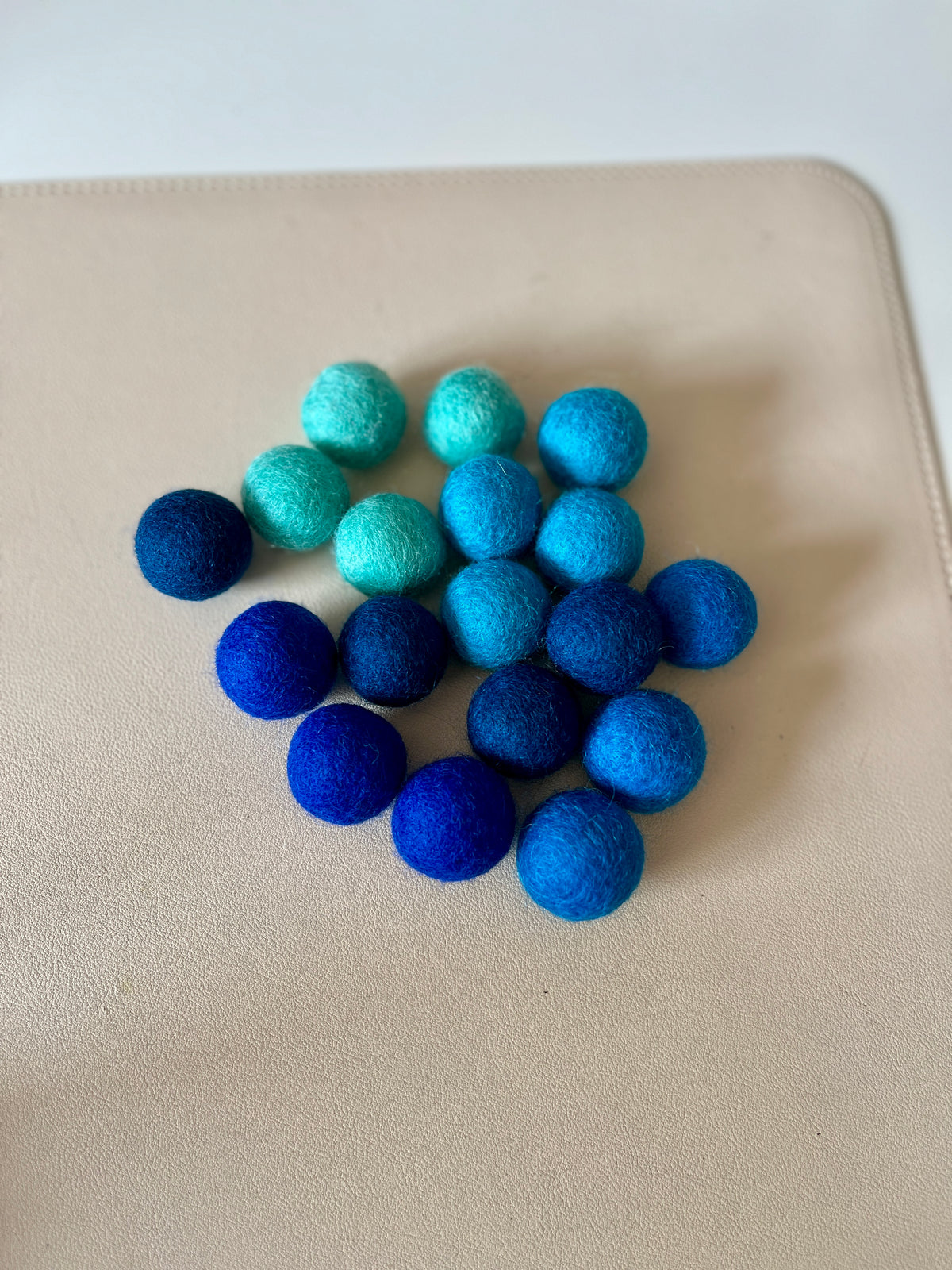 Assortment of multi blue felt balls in varying shades arranged on a neutral surface