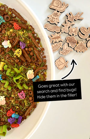 Plastic and wooden insect shapes scattered beside a bowl filled with textured grass and pasta mix on white surface