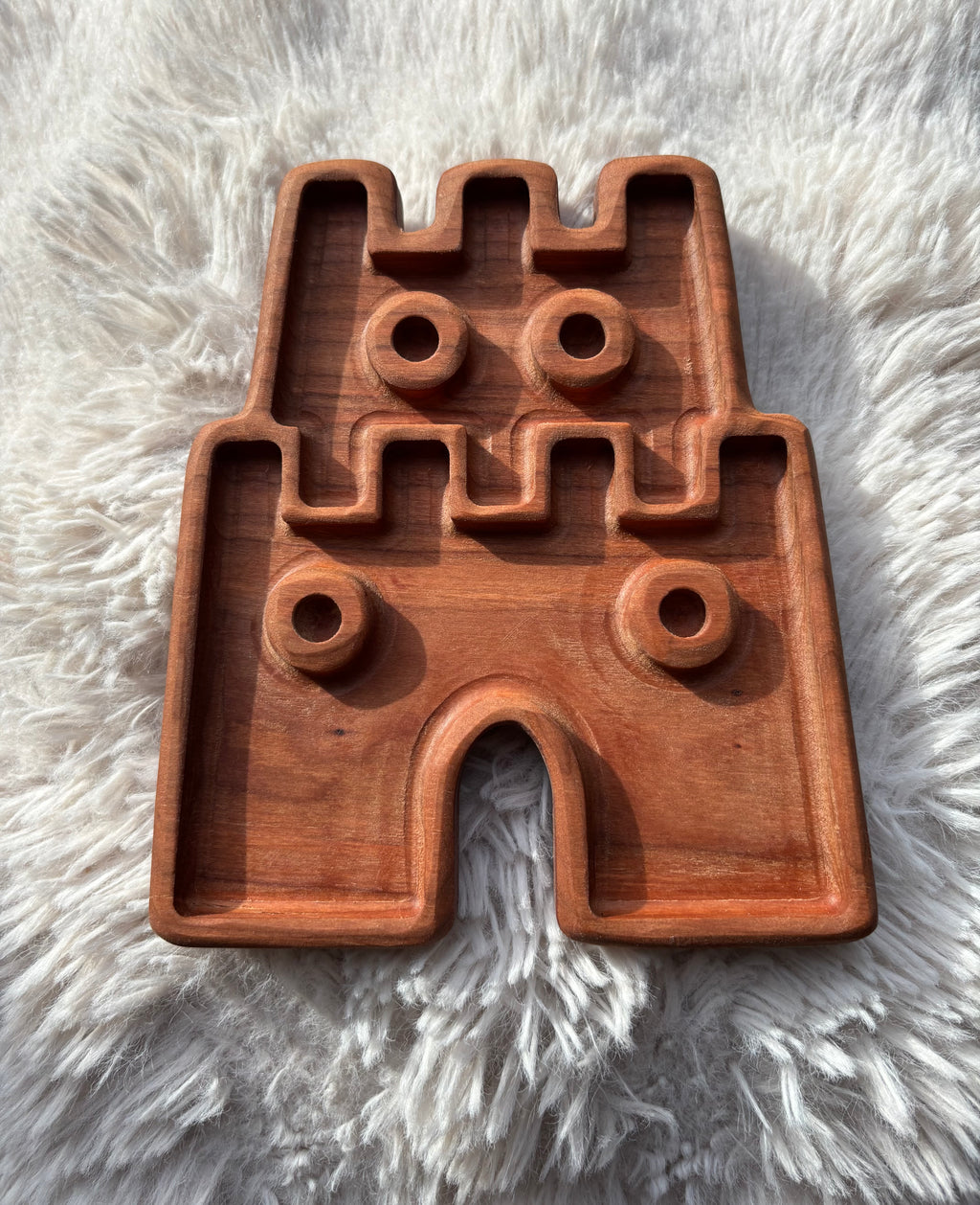 Carved wooden tray shaped like a castle with circular indentations on a soft white fur background