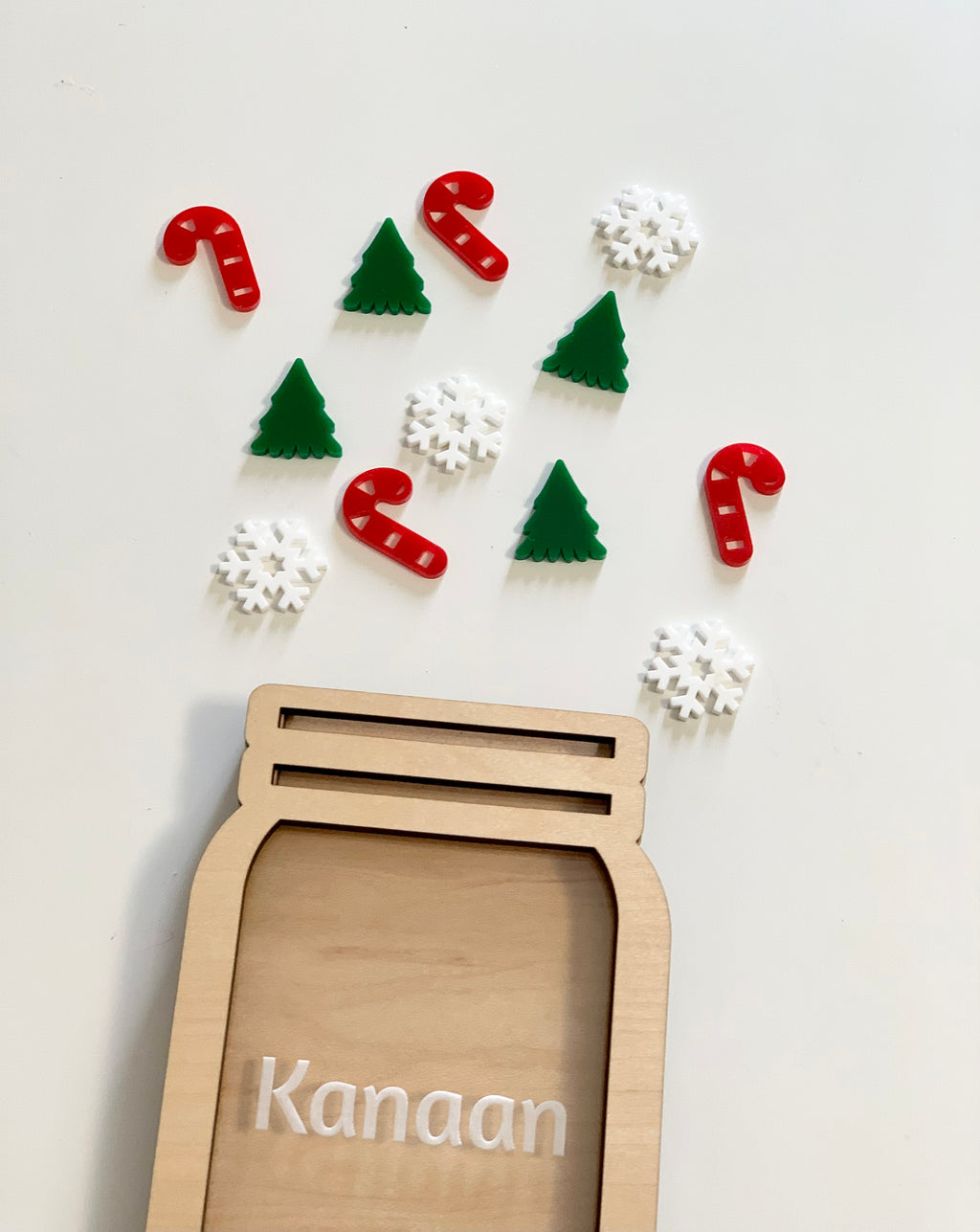 Wooden jar-shaped reward holder with personalized name and scattered festive candy cane, tree, and snowflake tokens on white background