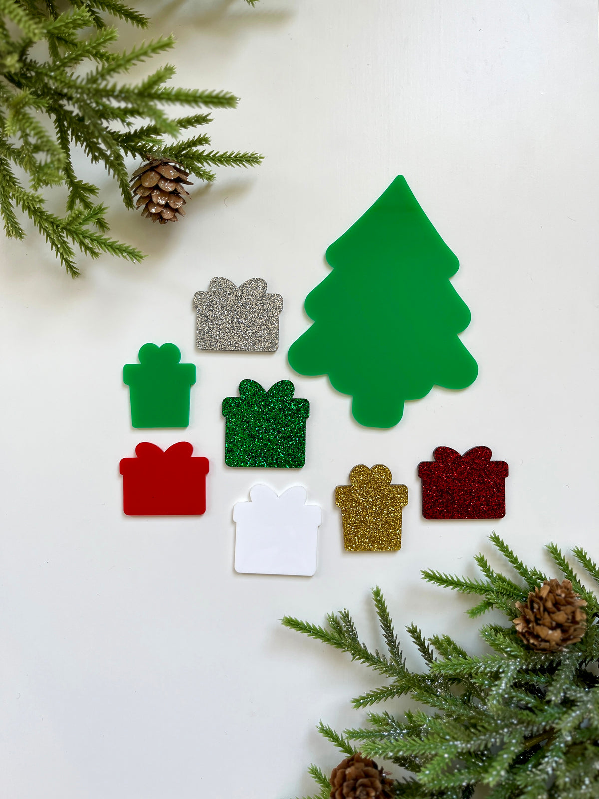 Green Christmas tree-shaped cutout surrounded by green, red, white, gold, and silver glittery present shapes on white background