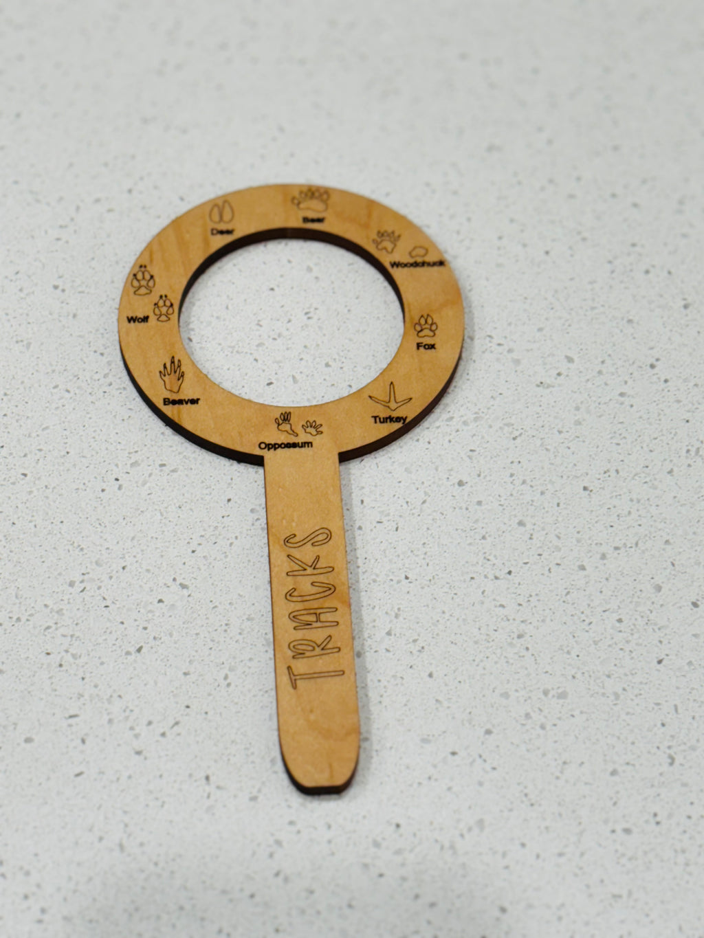 Circular wooden wildlife track identification tool with engraved animal tracks and names on a light speckled surface
