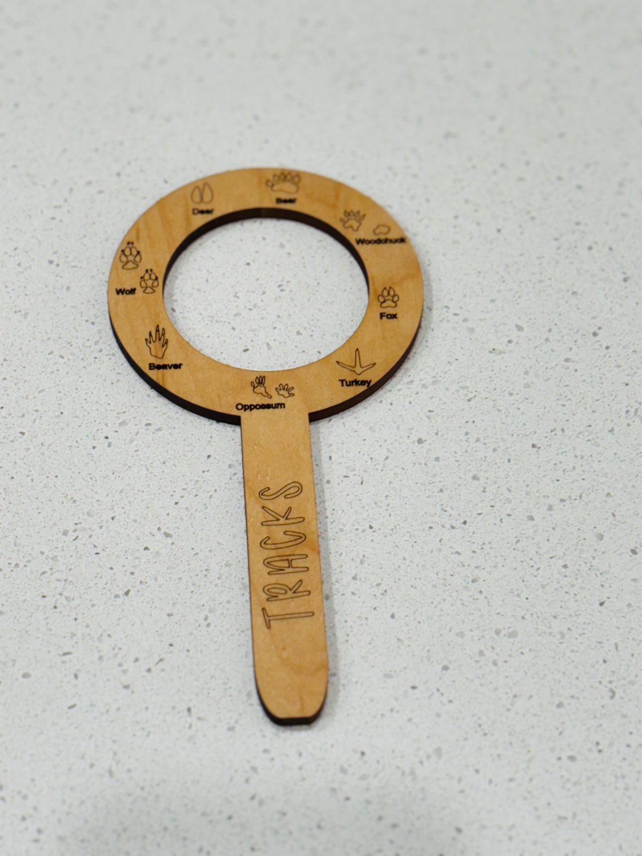 Circular wooden wildlife track identification tool with engraved animal tracks and names on a light speckled surface