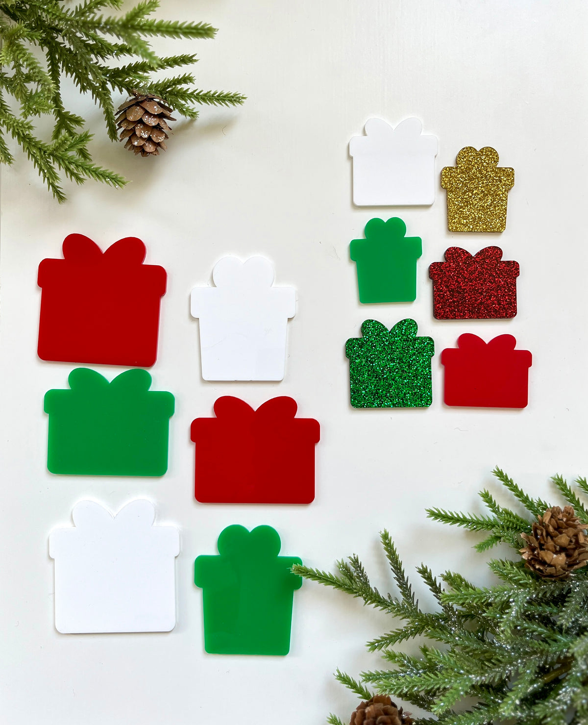 Assorted red, green, white, and glittery gold and red gift-shaped cutouts with pine branches and pinecones on white background