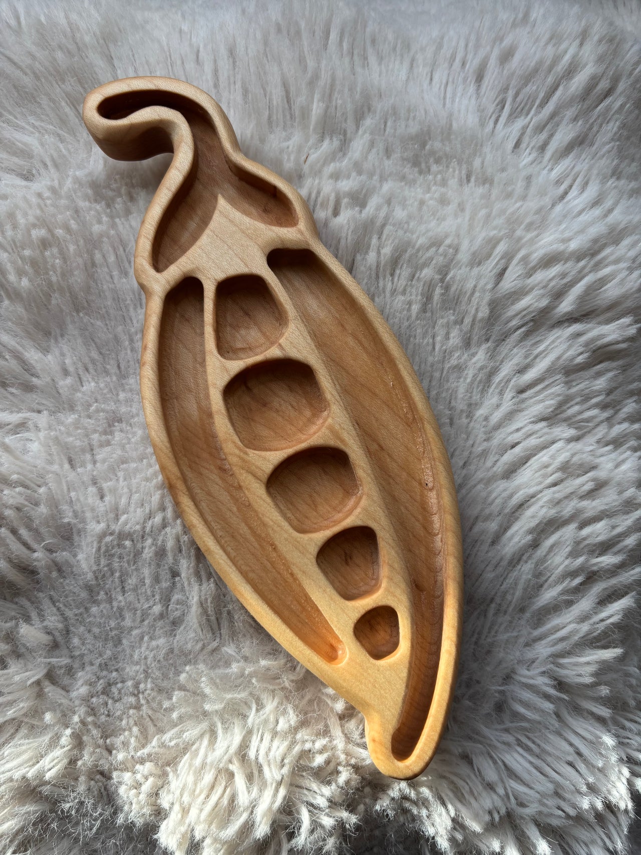 Carved wooden tray shaped like a pea pod with separate compartments on a soft textured fabric background