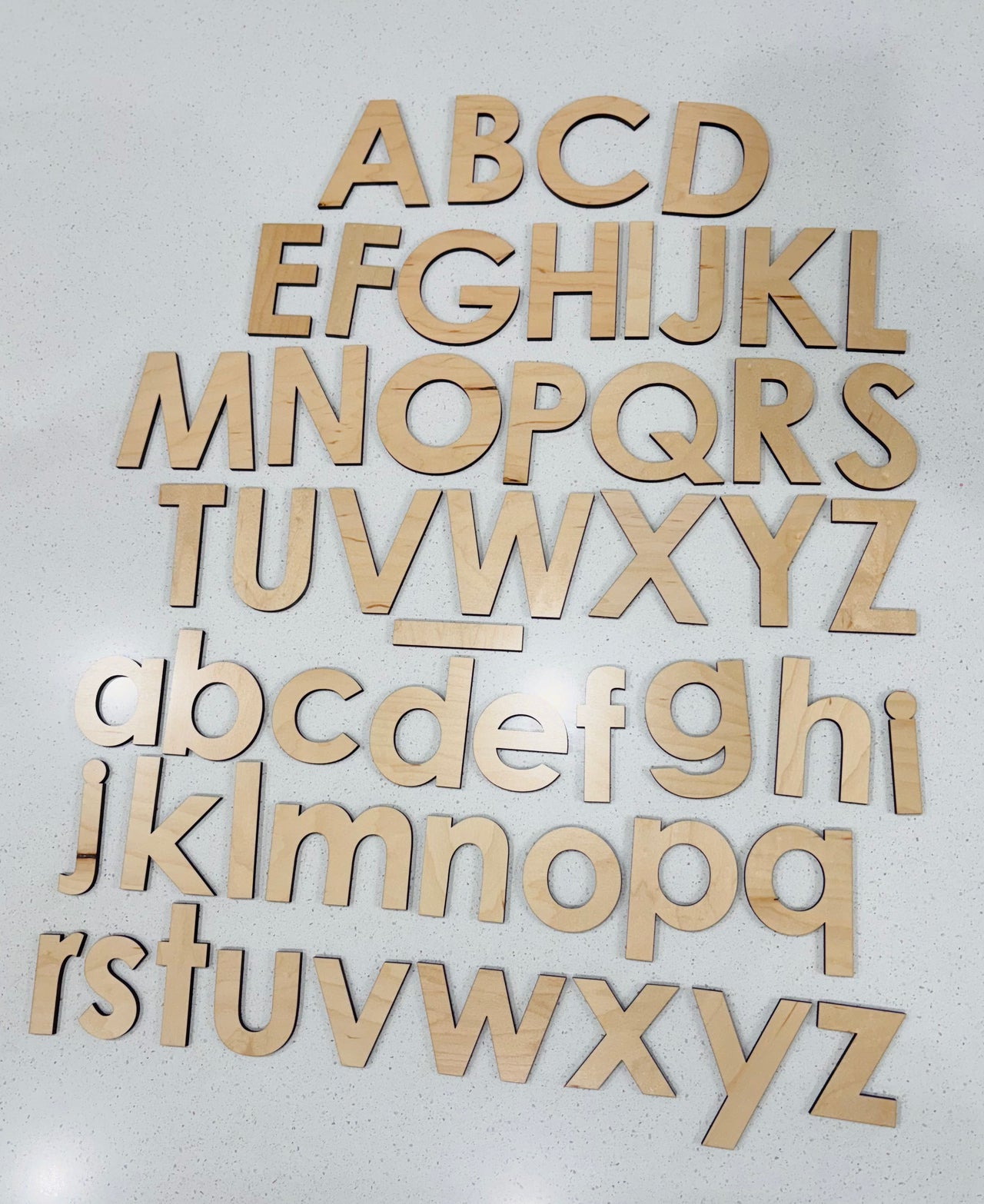 Uppercase and lowercase wooden alphabet letters arranged on a white speckled surface in rows