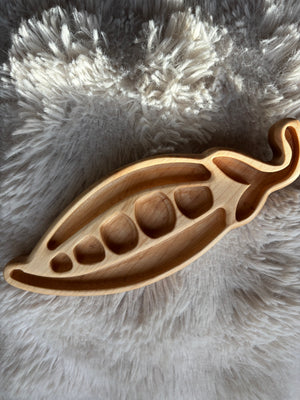 Light wooden tray shaped like a pea pod with curved compartments on a fluffy beige fabric background
