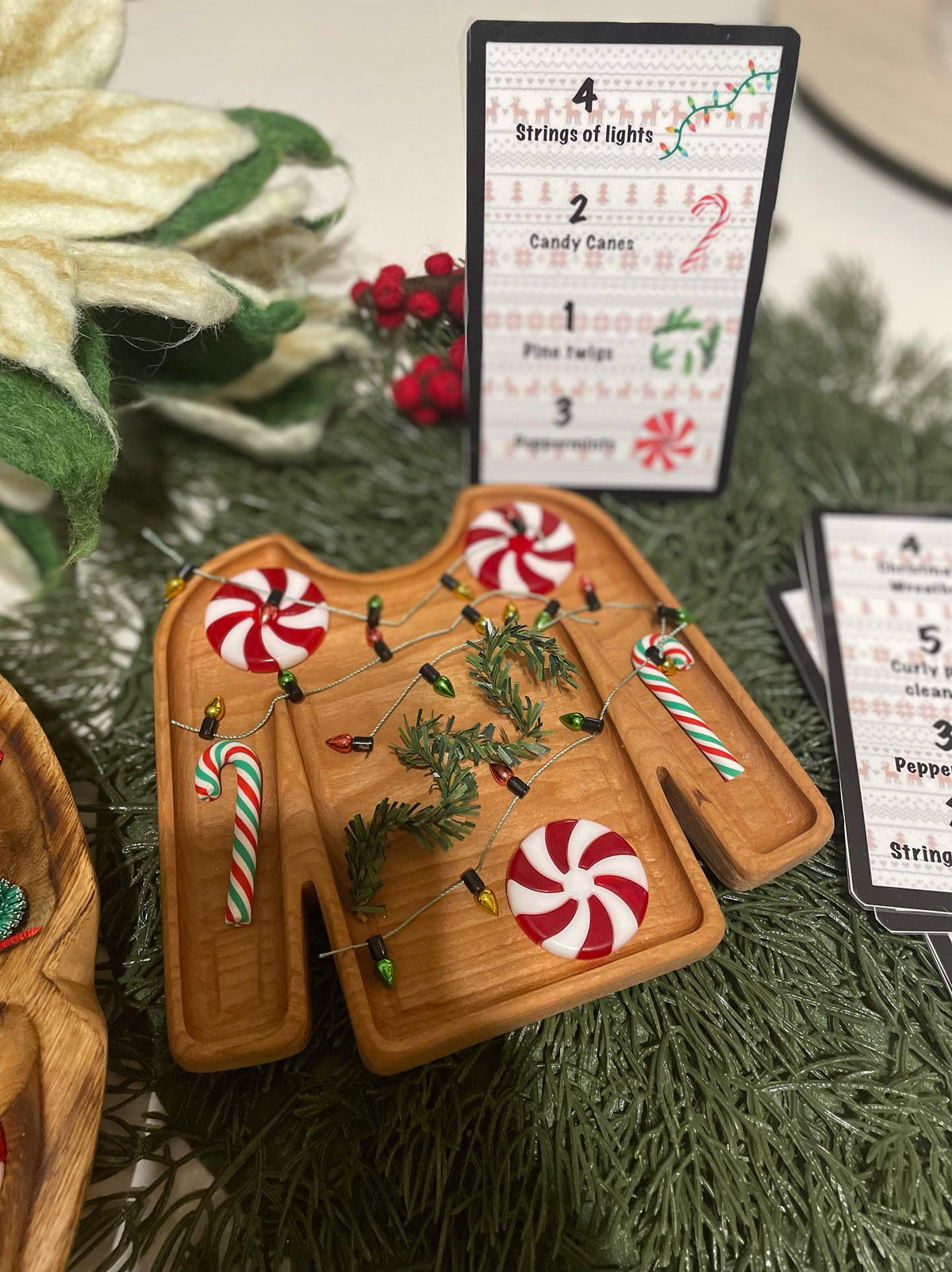 Wooden tray carved in the shape of a sweater decorated with peppermint swirls, candy canes, pine twigs, and string lights
