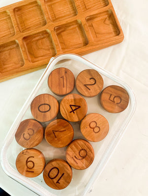 Clear zippered pouch holding wooden numbered discs arranged on a white surface with a wooden tray nearby