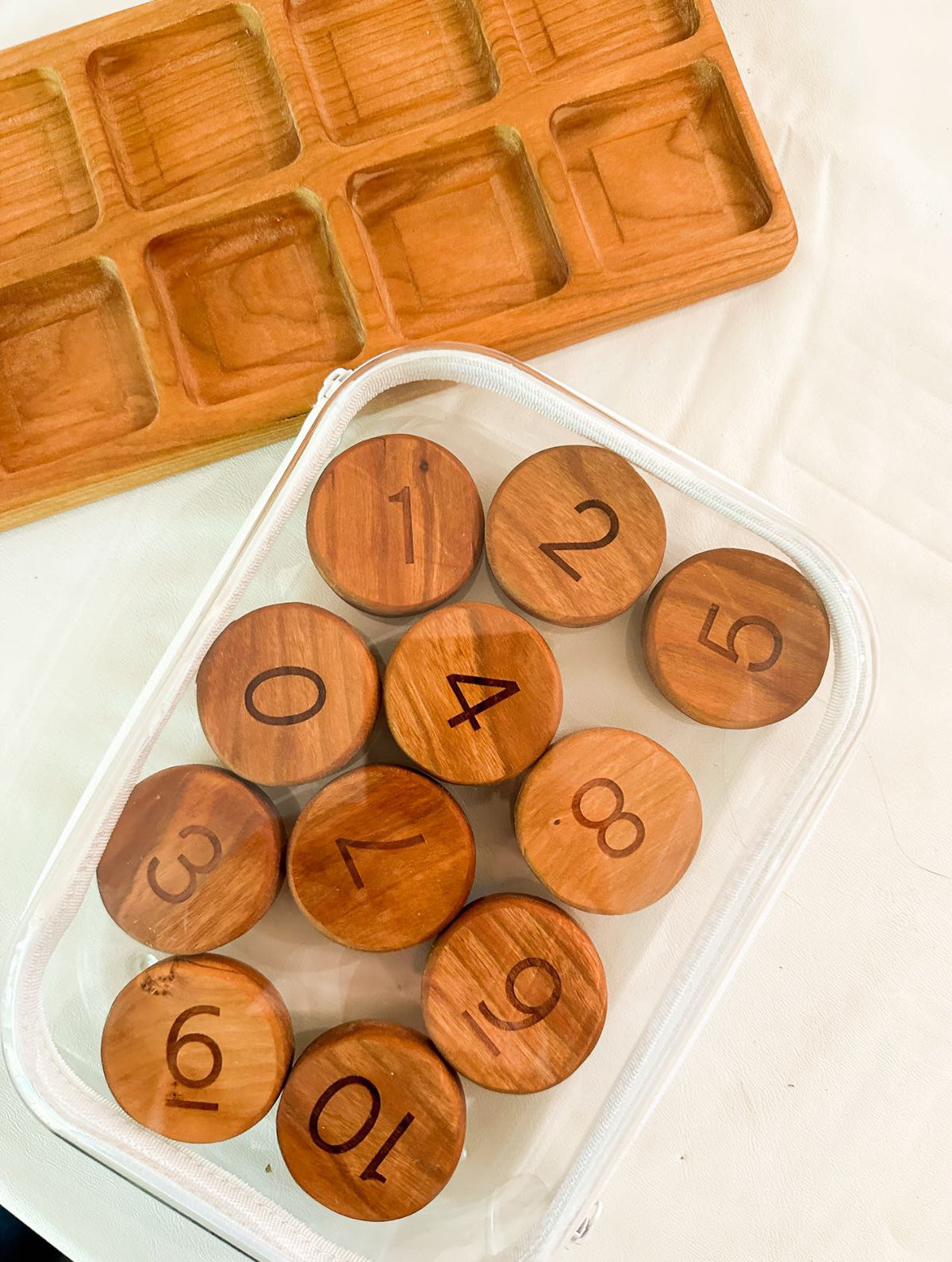 Clear zippered pouch holding wooden numbered discs arranged on a white surface with a wooden tray nearby