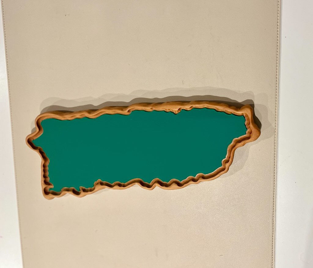 Wooden tray with contoured edges filled with green paint shaped like the island of Puerto Rico on a beige surface