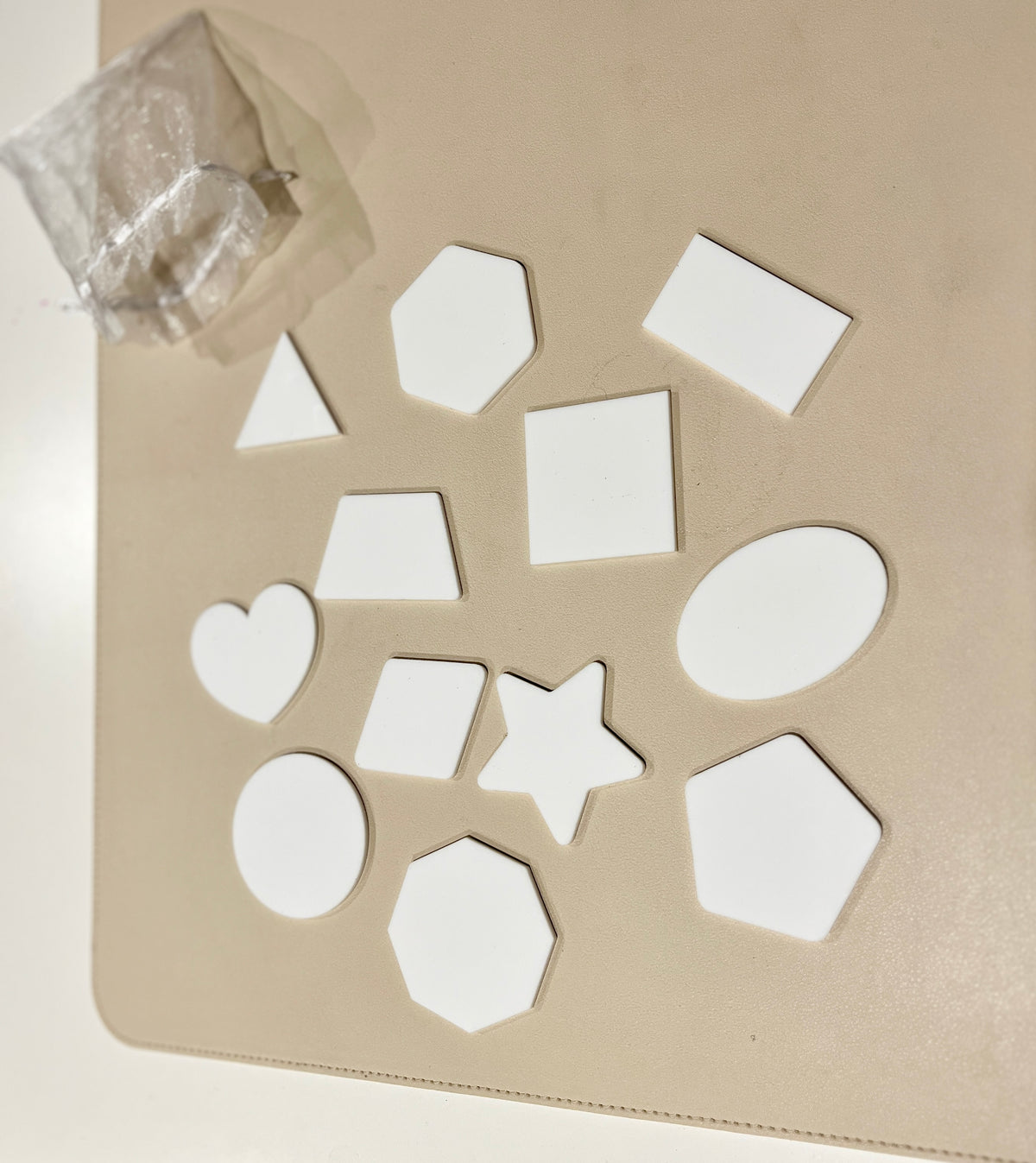 Assorted white wooden shapes including heart, star, hexagons, oval, circle, rectangle, square, and triangle on a beige surface