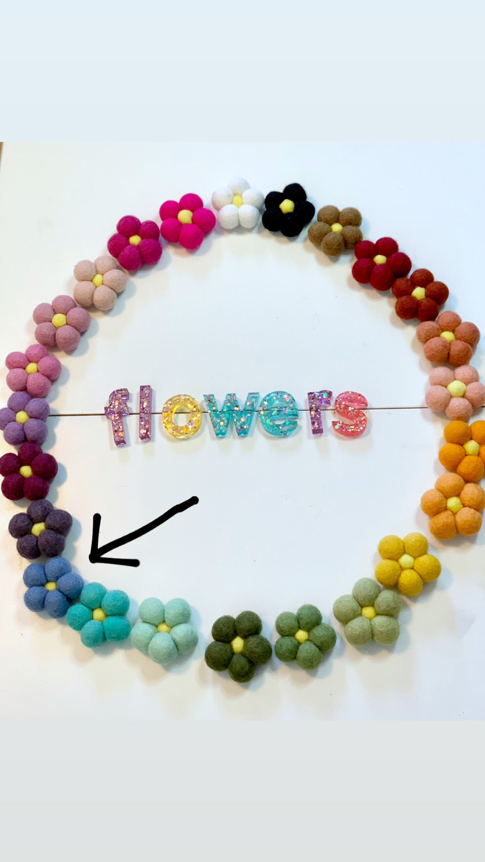 Circular arrangement of colorful handmade felt flowers with colorful glitter letters spelling flowers in the center