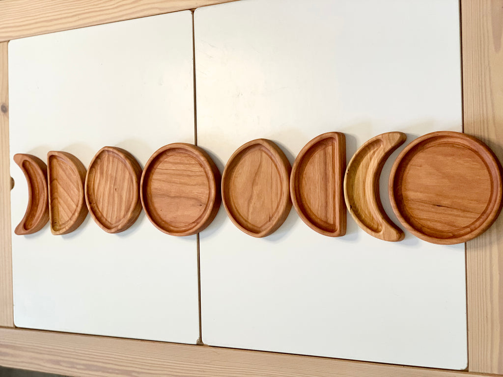 Set of wooden moon phase sensory plates arranged in order on white surface with natural wood background