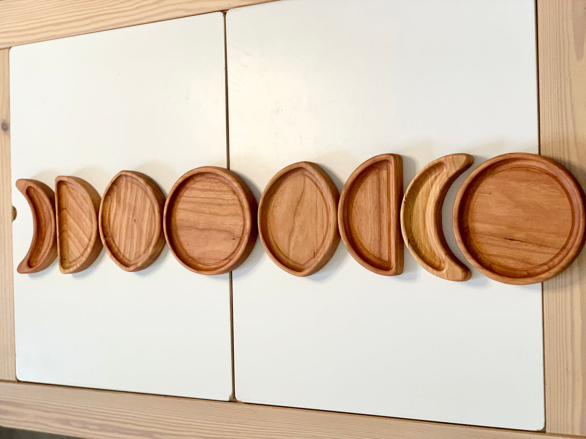 Set of wooden moon phase sensory plates arranged in order on white surface with natural wood background