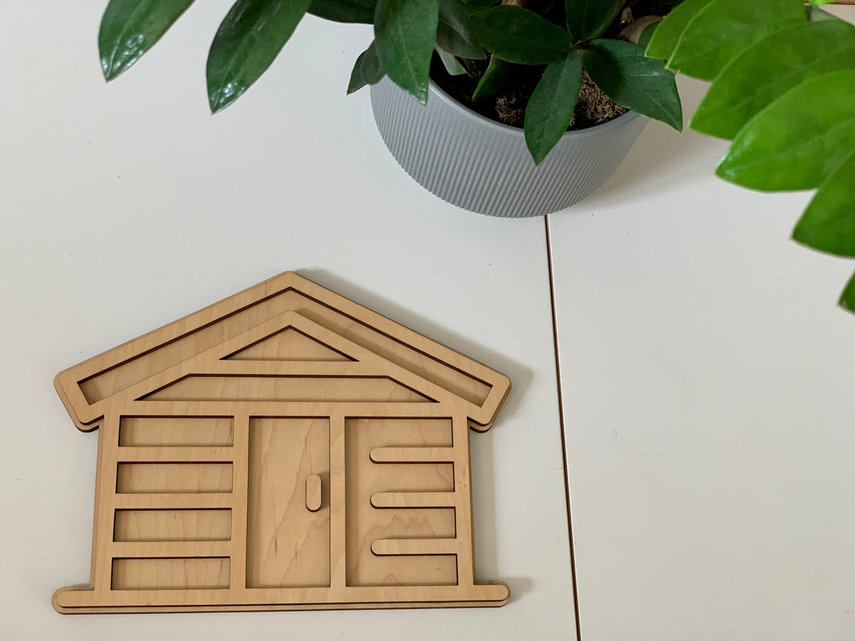 Maple plywood fillable log home play tray with geometric cutouts on white table next to green potted plant