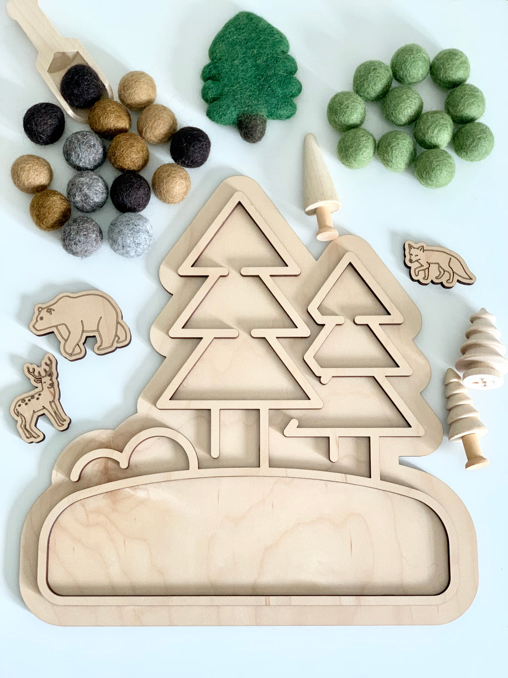 Wooden fillable woodland play tray with tree-shaped compartments, felt balls, wooden animal figures, and wooden spoons on white surface