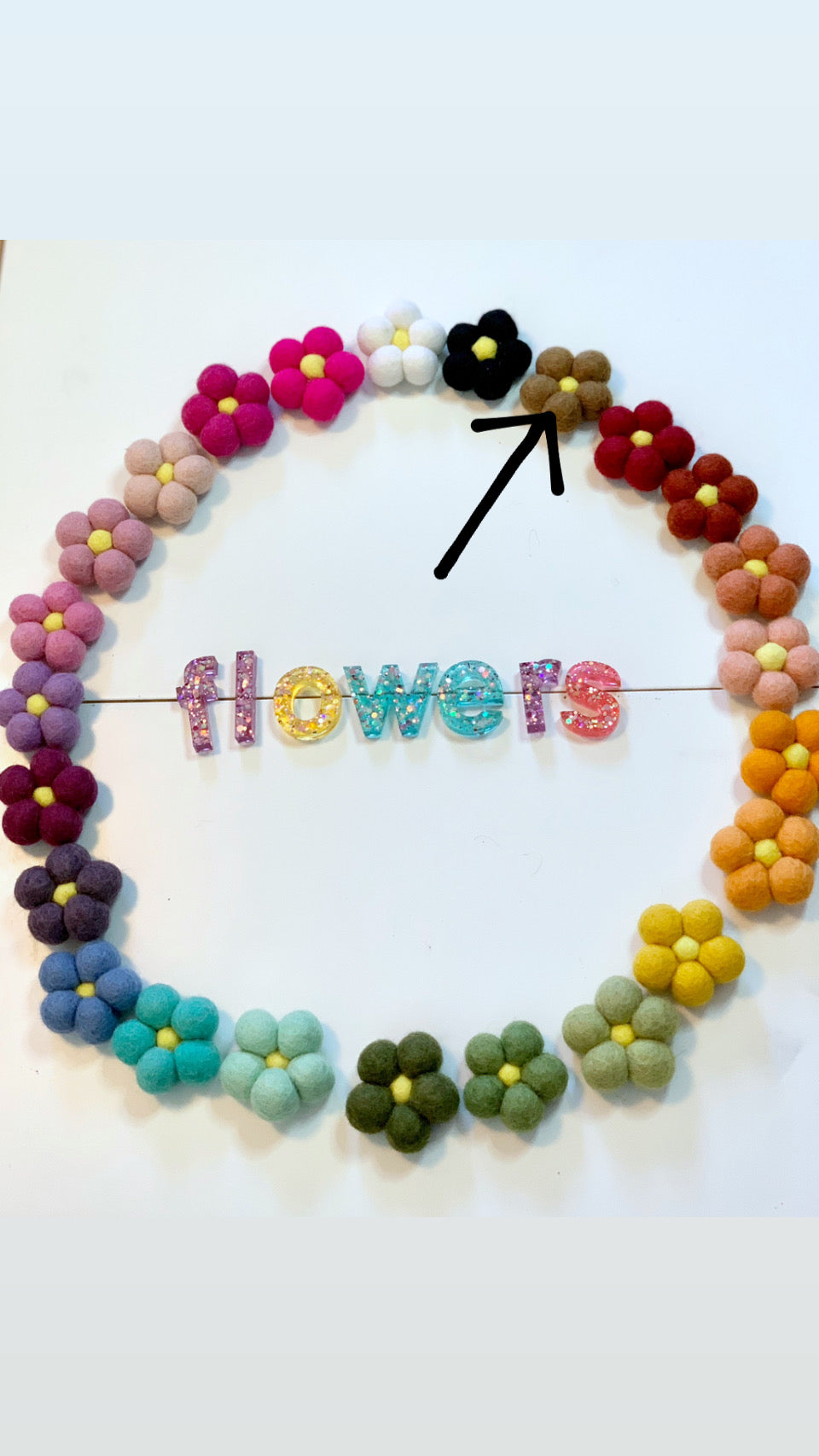 Single handmade felt flower in tan with yellow center surrounded by multicolored felt flowers and glitter letters spelling flowers