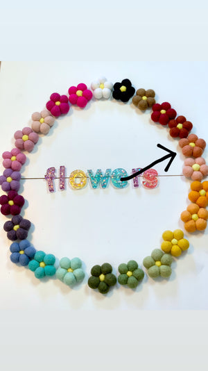 Colorful handmade felt flowers arranged in a circle with glittery letters spelling flowers on white background