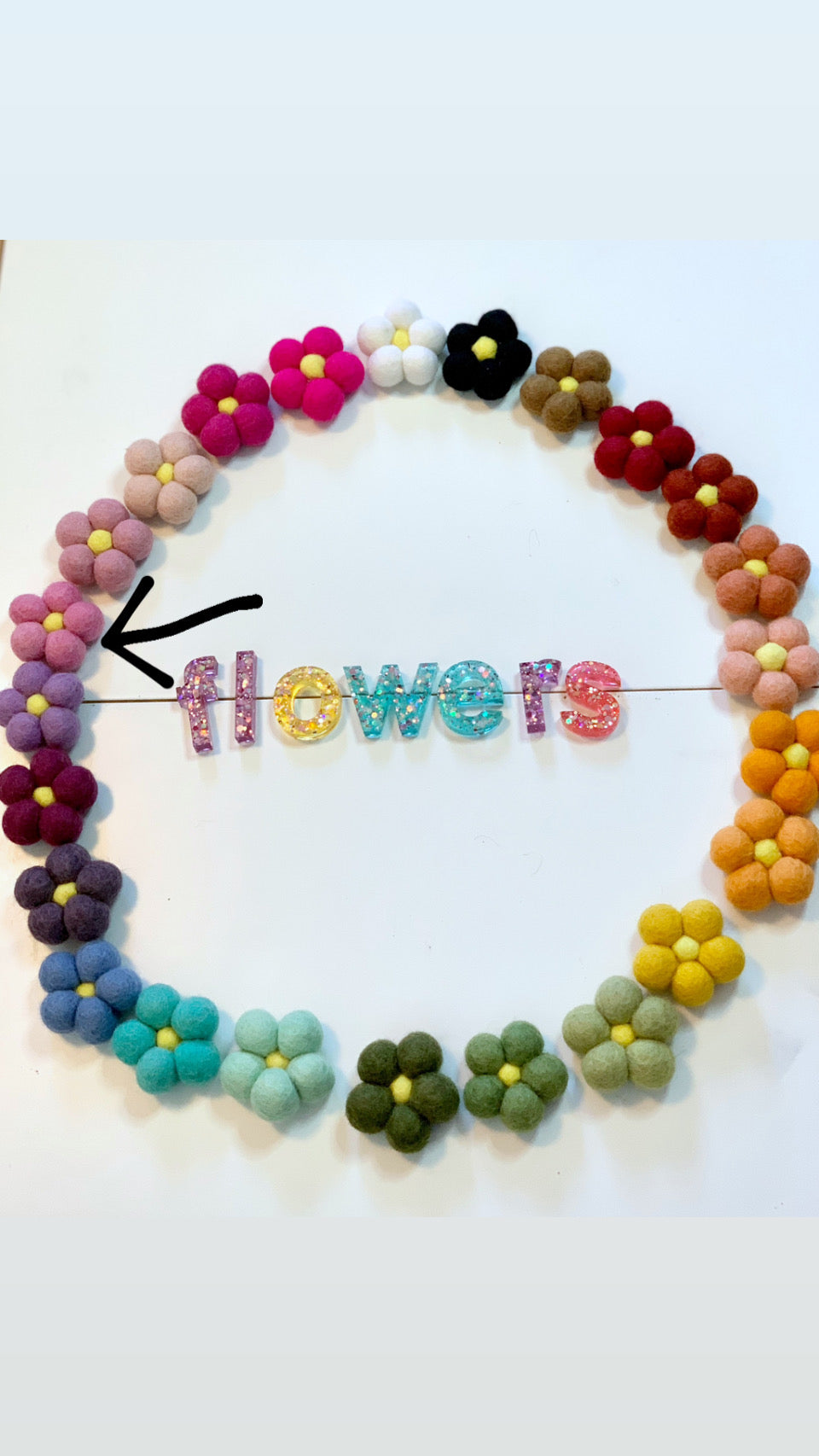 Single handmade felt flower in soft purple with yellow center surrounded by colorful felt flowers on white background