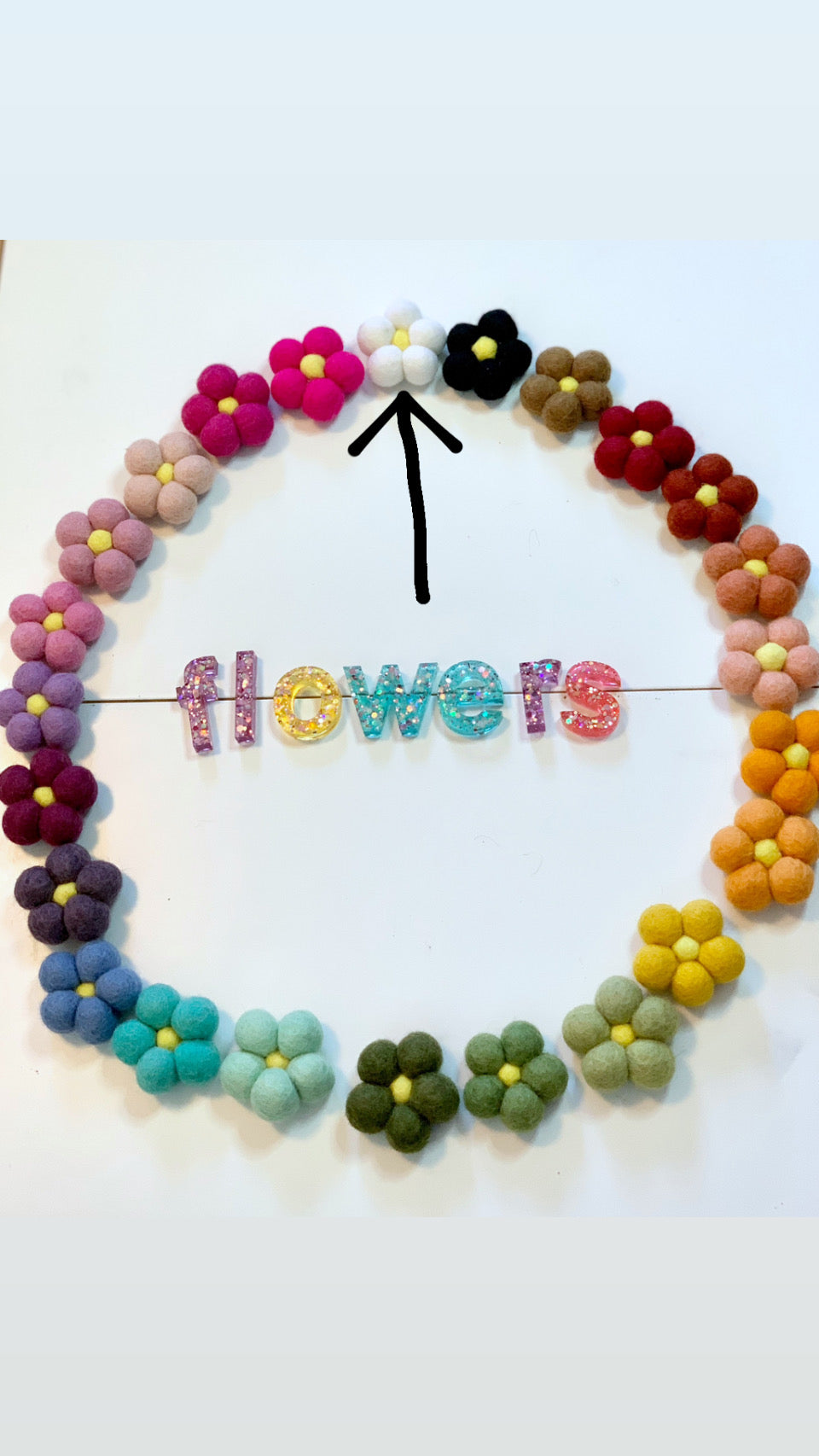 Single handmade felt flower in white wool with yellow center among multicolored felt flowers on white background