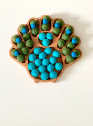 Wooden peacock-shaped sensory tray with green and blue felt balls arranged in tail feather compartments on white background