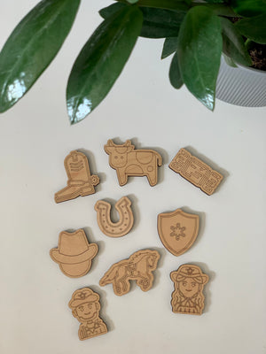 Laser cut wooden western-themed loose parts set with cowboy hat, horse, cow, horseshoe, sheriff badge, and characters on white surface
