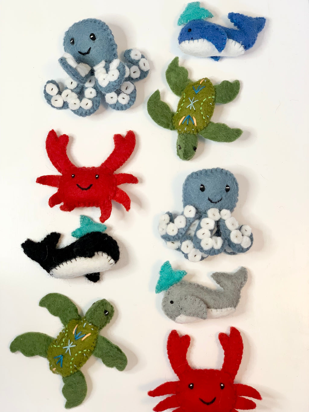 Handmade felt sea creatures including blue octopus, red crab, green turtle, blue shark, black whale, and gray whale on white background