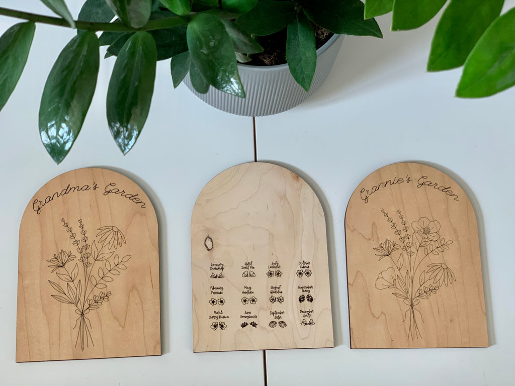 Set of three personalized wooden garden plaques with floral designs and birth month symbols on white surface