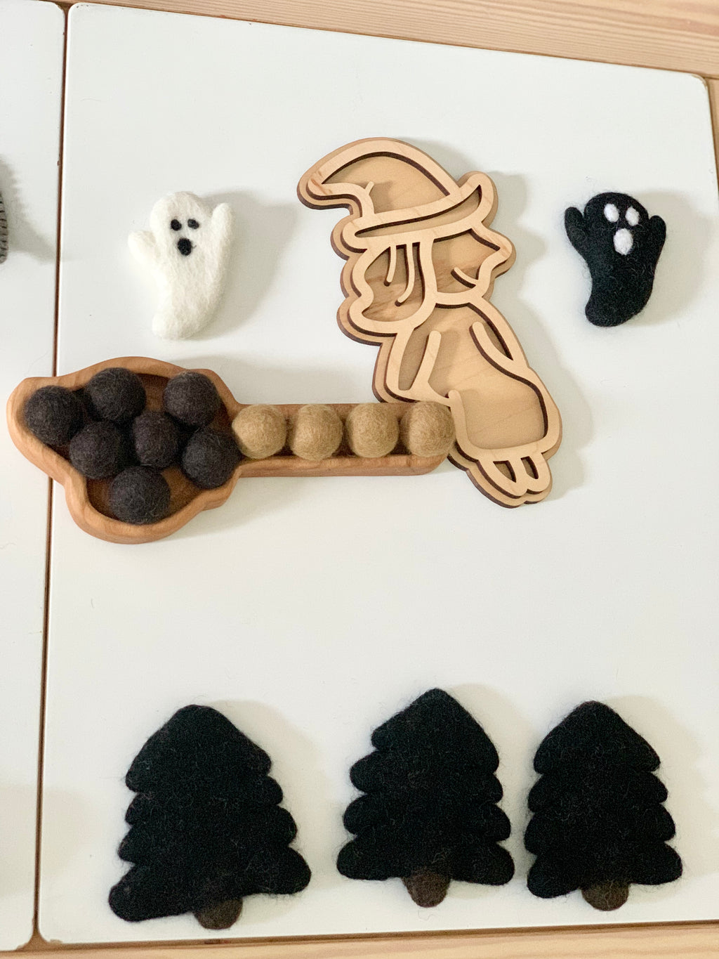 Wooden fillable witch-shaped play tray with felt black and brown balls, felt ghost and paw, and black felt trees on white table