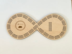 Wooden infinity-shaped crib board with engraved AW and Co logo and scoring holes for 8 pegs on white background