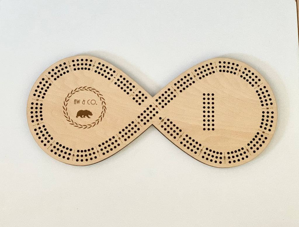 Wooden infinity-shaped crib board with engraved AW and Co logo and scoring holes for 8 pegs on white background