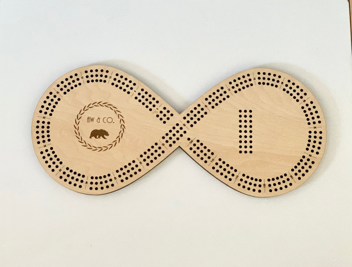 Wooden infinity-shaped crib board with engraved AW and Co logo and scoring holes for 8 pegs on white background