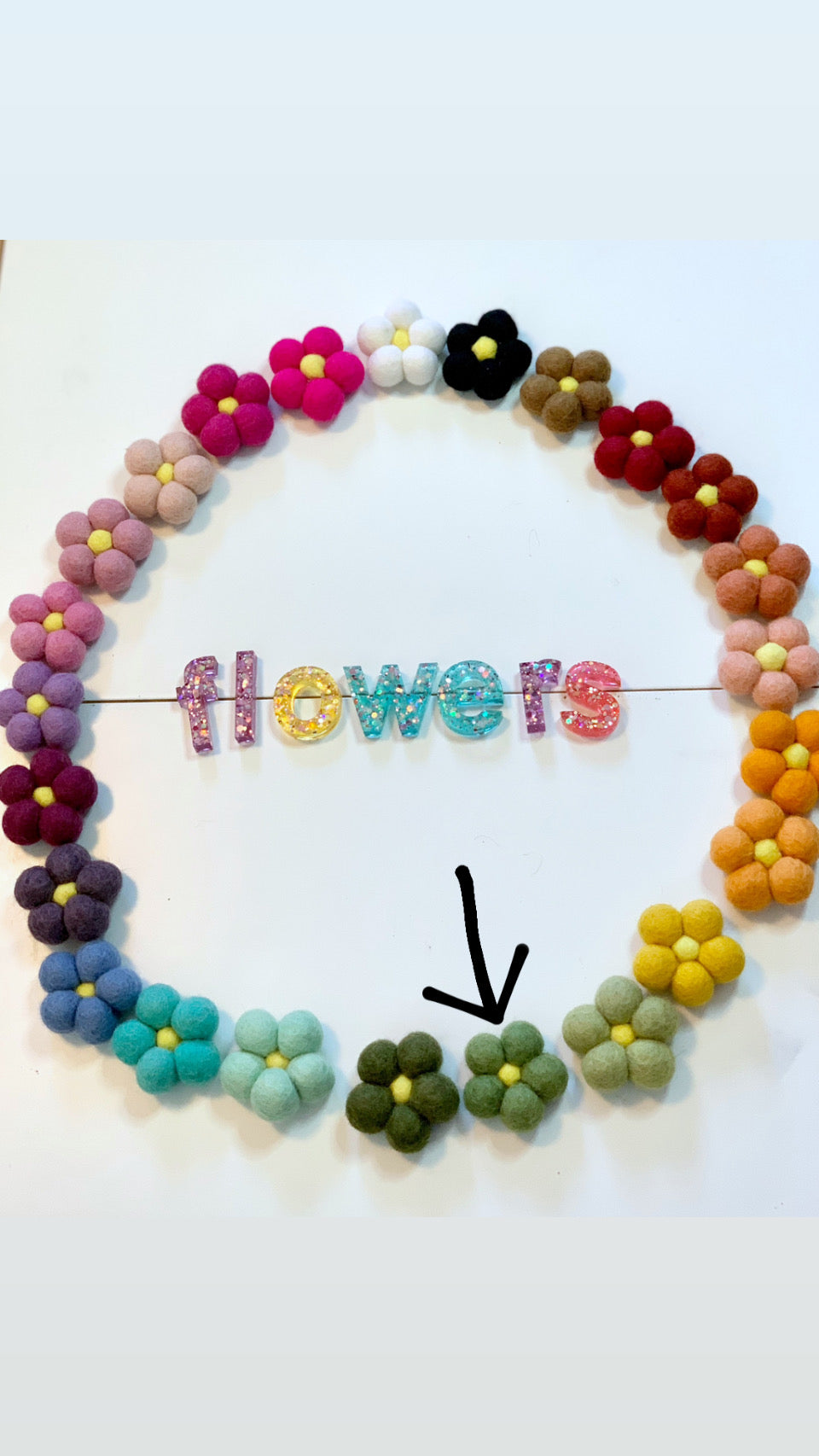 Circle of colorful felt flowers arranged around glittery letters spelling flowers with black arrow pointing to green flowers