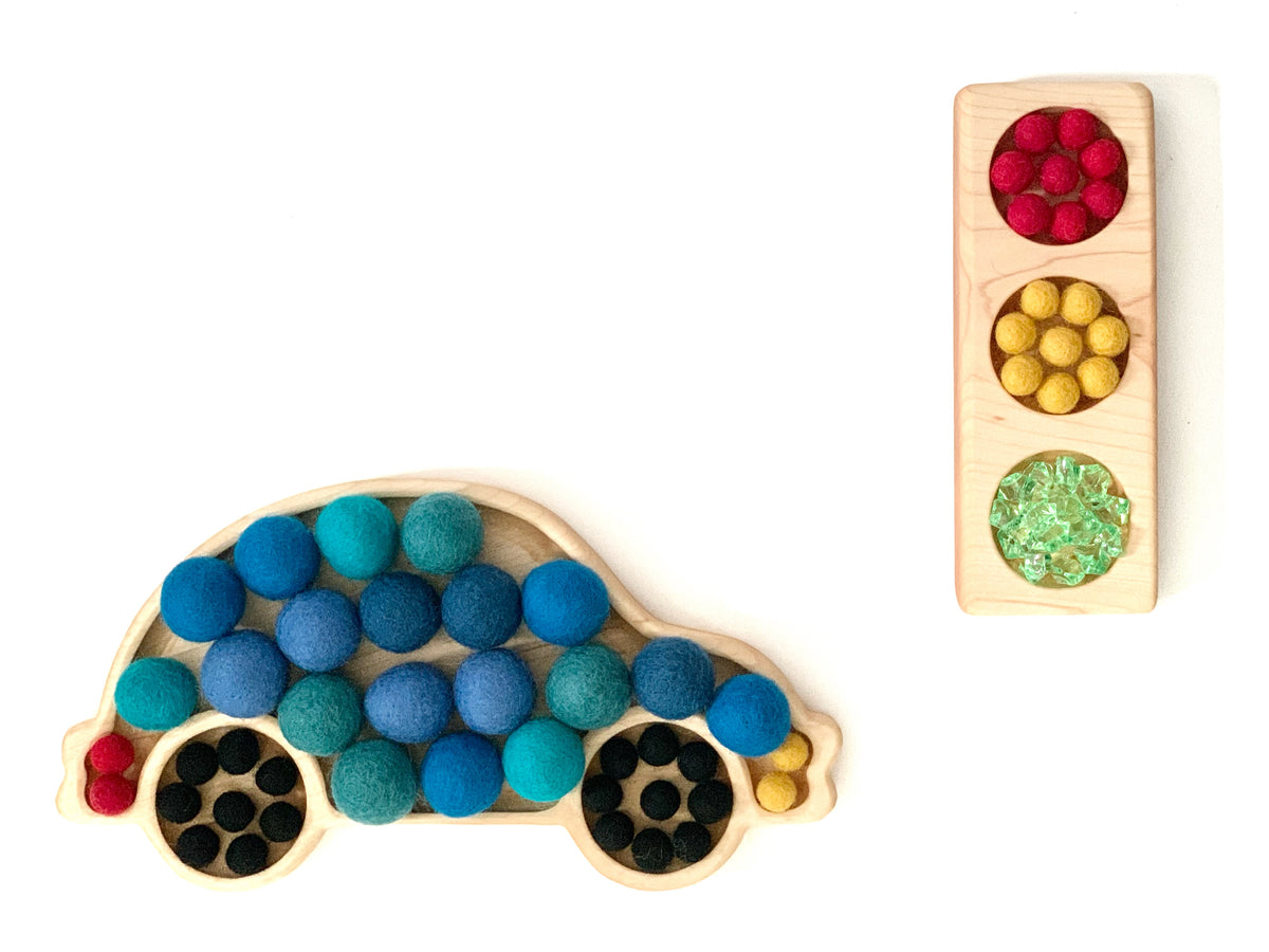 Wooden car-shaped sensory tray filled with blue and teal felt balls and a rectangular tray with red, yellow felt balls and green beads